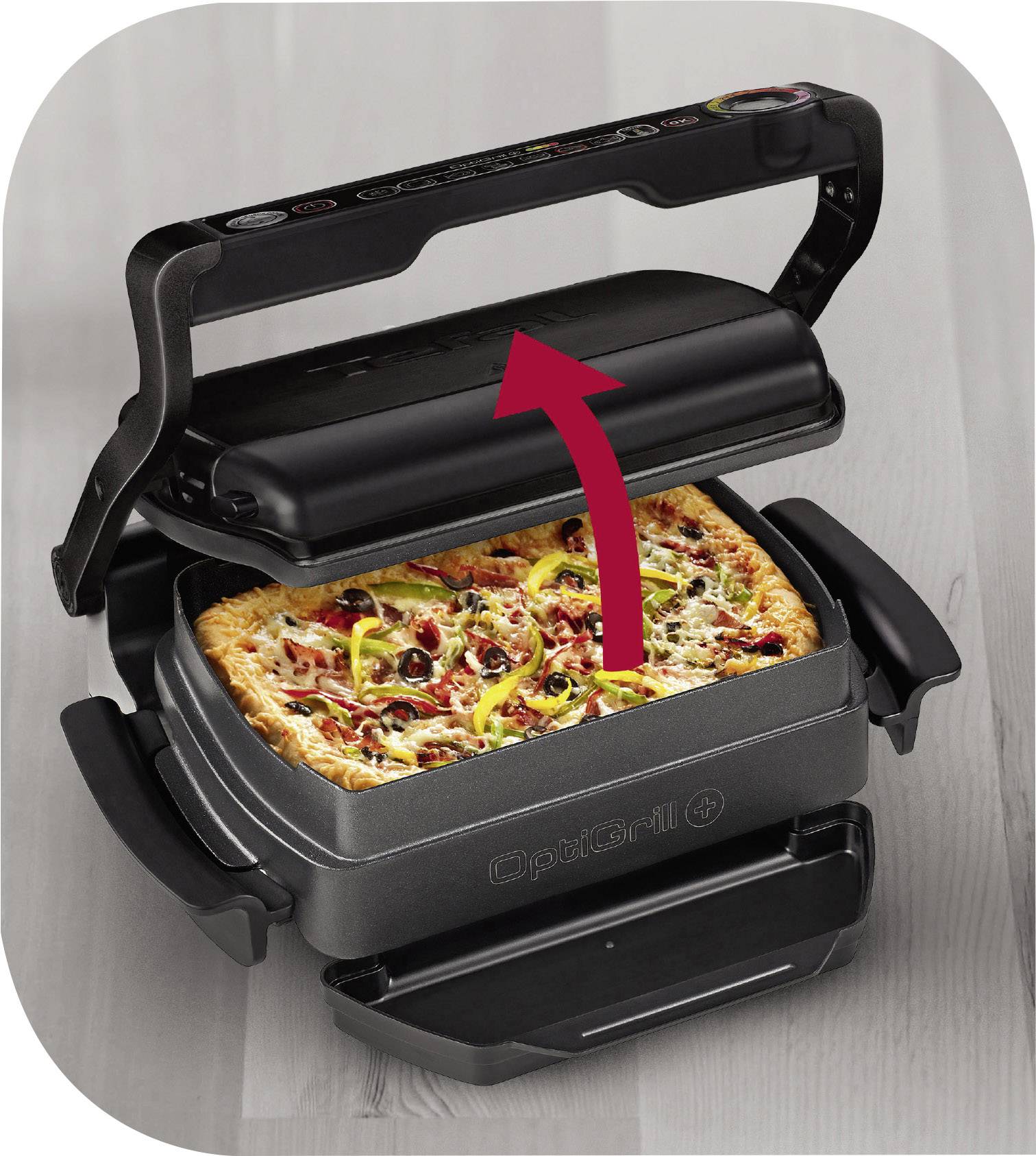 Kontaktní gril, který peče pizzu s pepperoni a olivami. Červená šipka ukazuje na rukojeť grilu, která se otevírá.