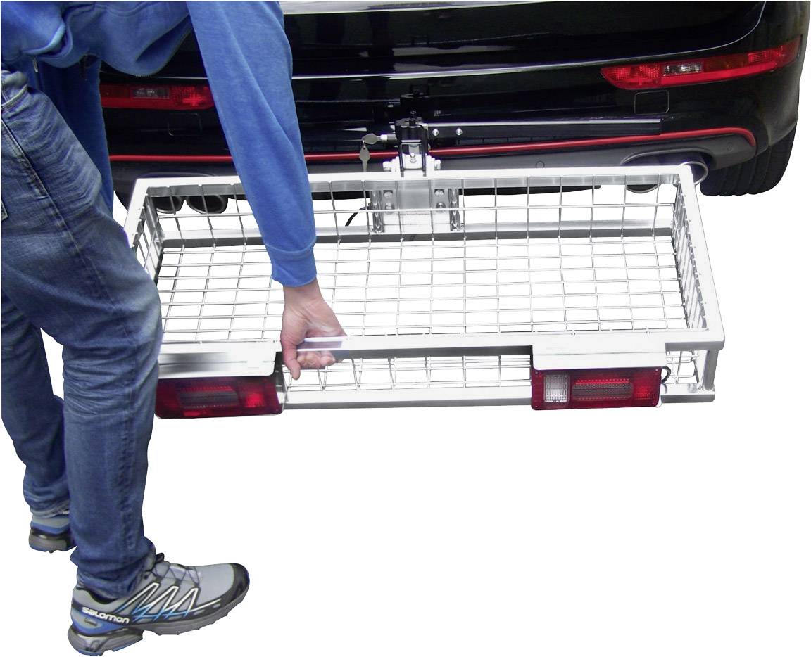 Osoba v džínách a modrých botách montuje nosič zavazadel na zadní části černého automobilu.
