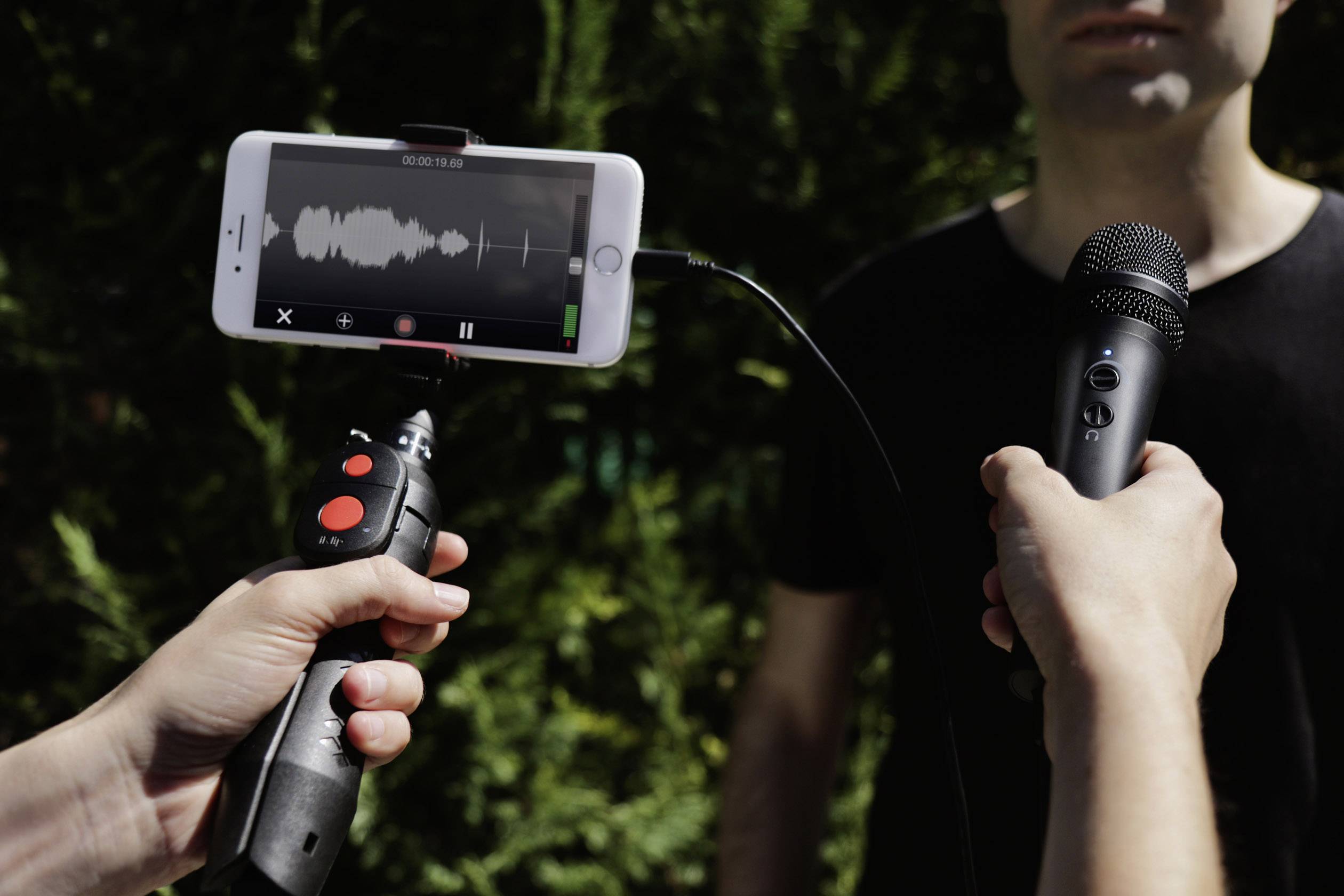Osoba je interviewována venku. Smartphone je připojeno k mikrofonu pro nahrávání zvuku.