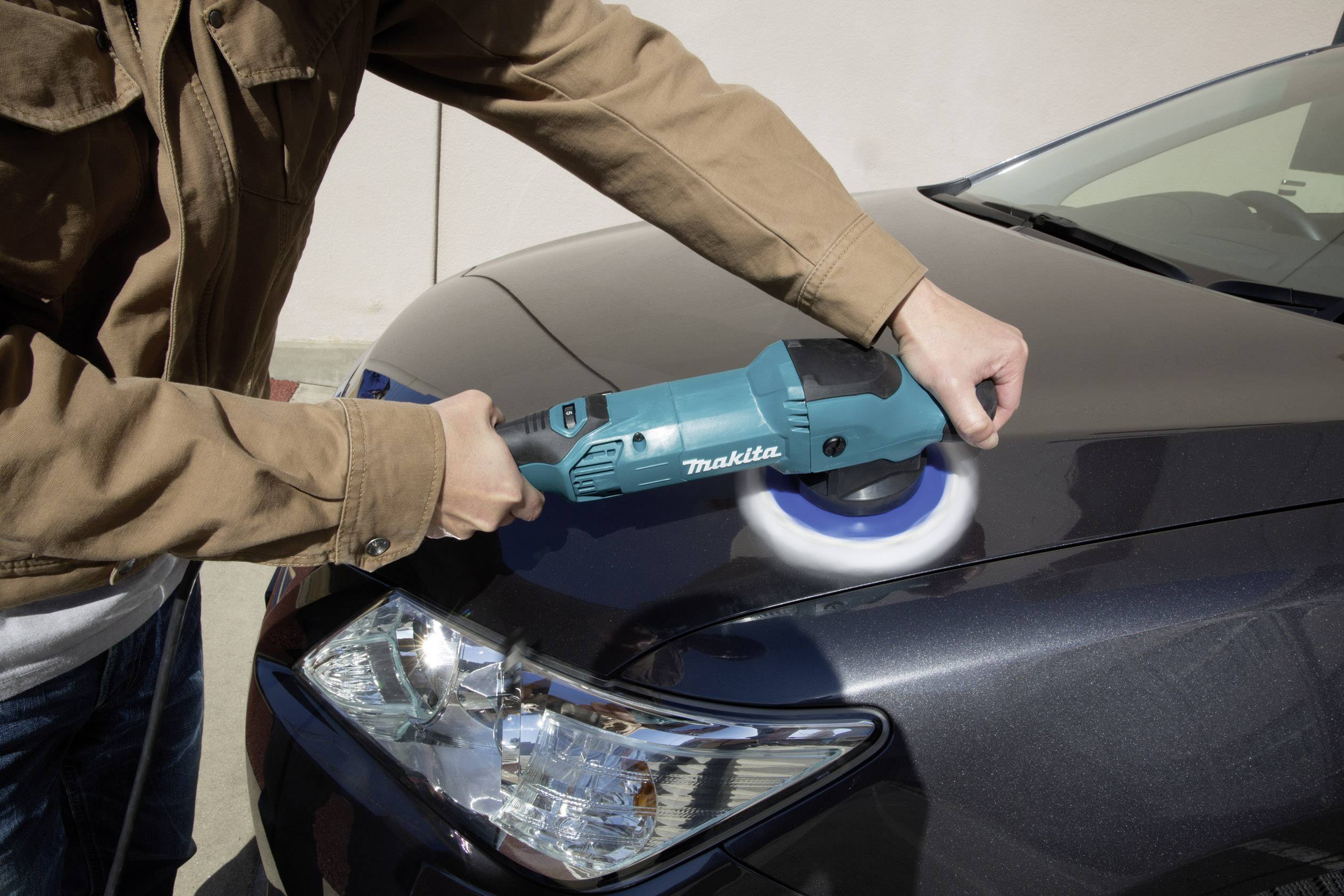 Muž leští auto modrým nástrojem na kapotě. Lak se stává lesklým a čistým.
