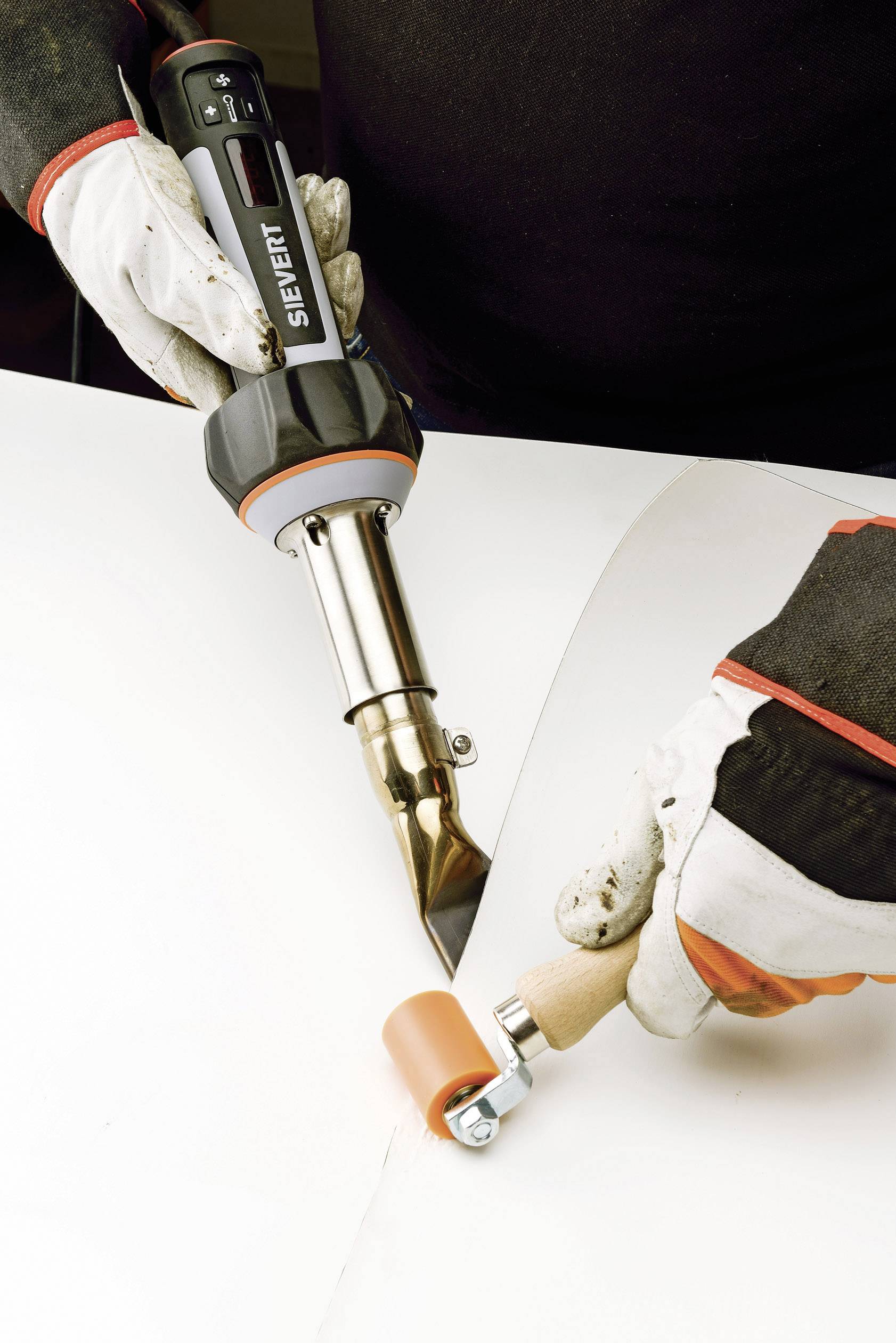 Tepelné utěsnění dvou fólií. Jedna osoba drží horkovzdušný pistoli a přitlačuje fólie válečkovým nástrojem.