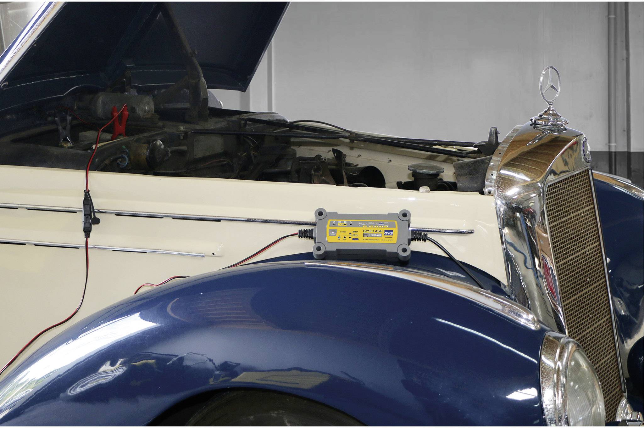 Staré auto s otevřenou kapotou motoru je nabíjeno nabíjecím zařízením.
