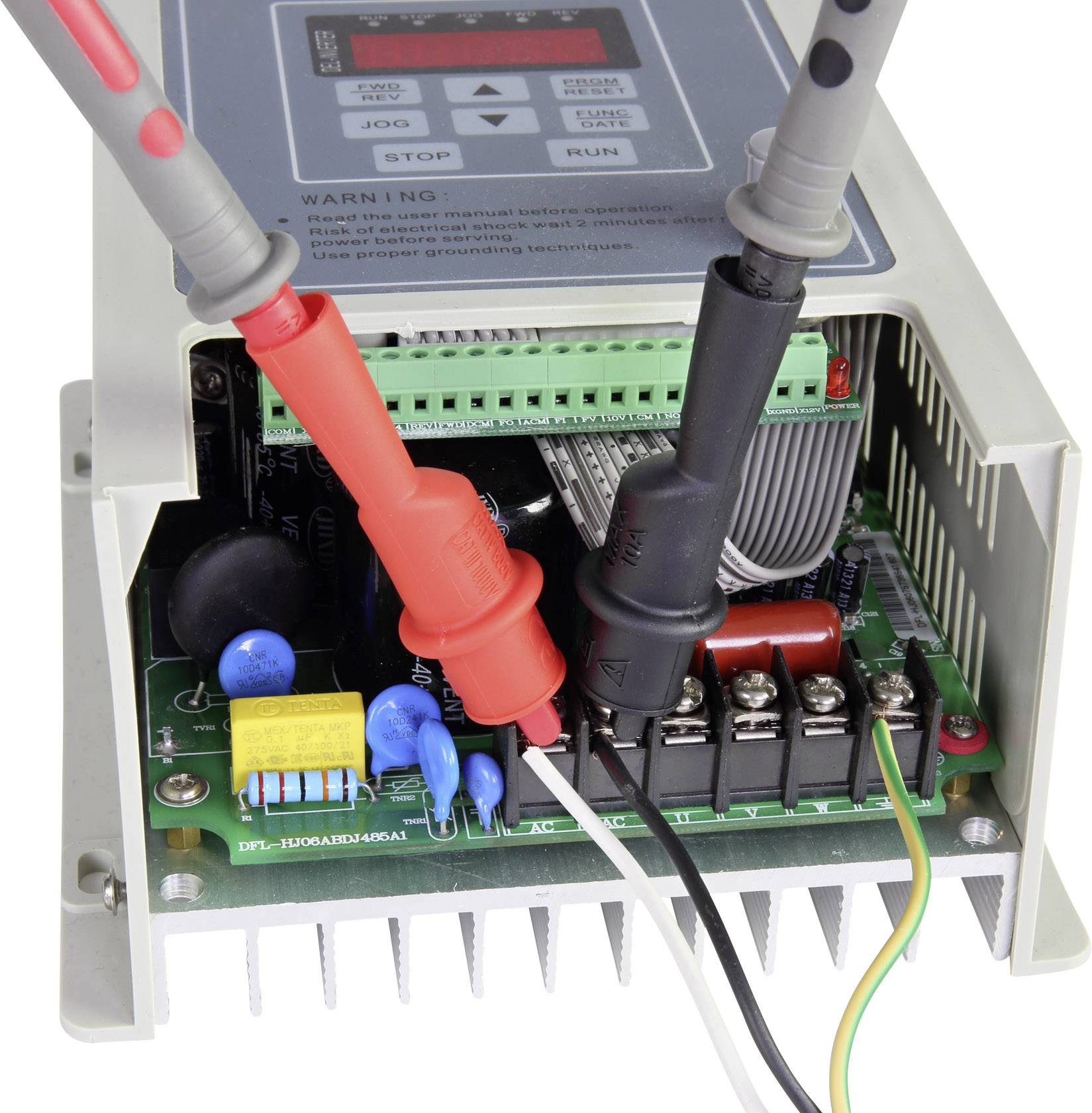 Otevřené elektronické zařízení s viditelnými obvody a dvěma připojenými měřicími vodiči (červenými a černými).