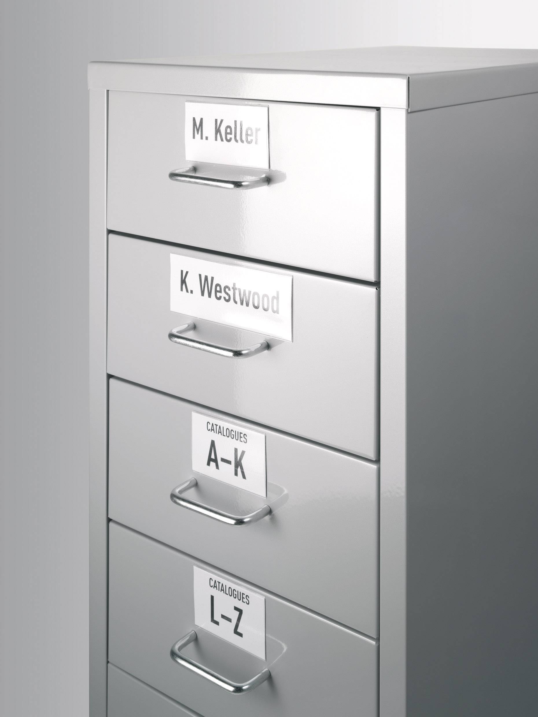Stříbrná kovová skříň se čtyřmi zásuvkami, označená shora dolů: 'M. Keller', 'K. Westwood', 'Katalogy A-K', 'Katalogy L-Z'.