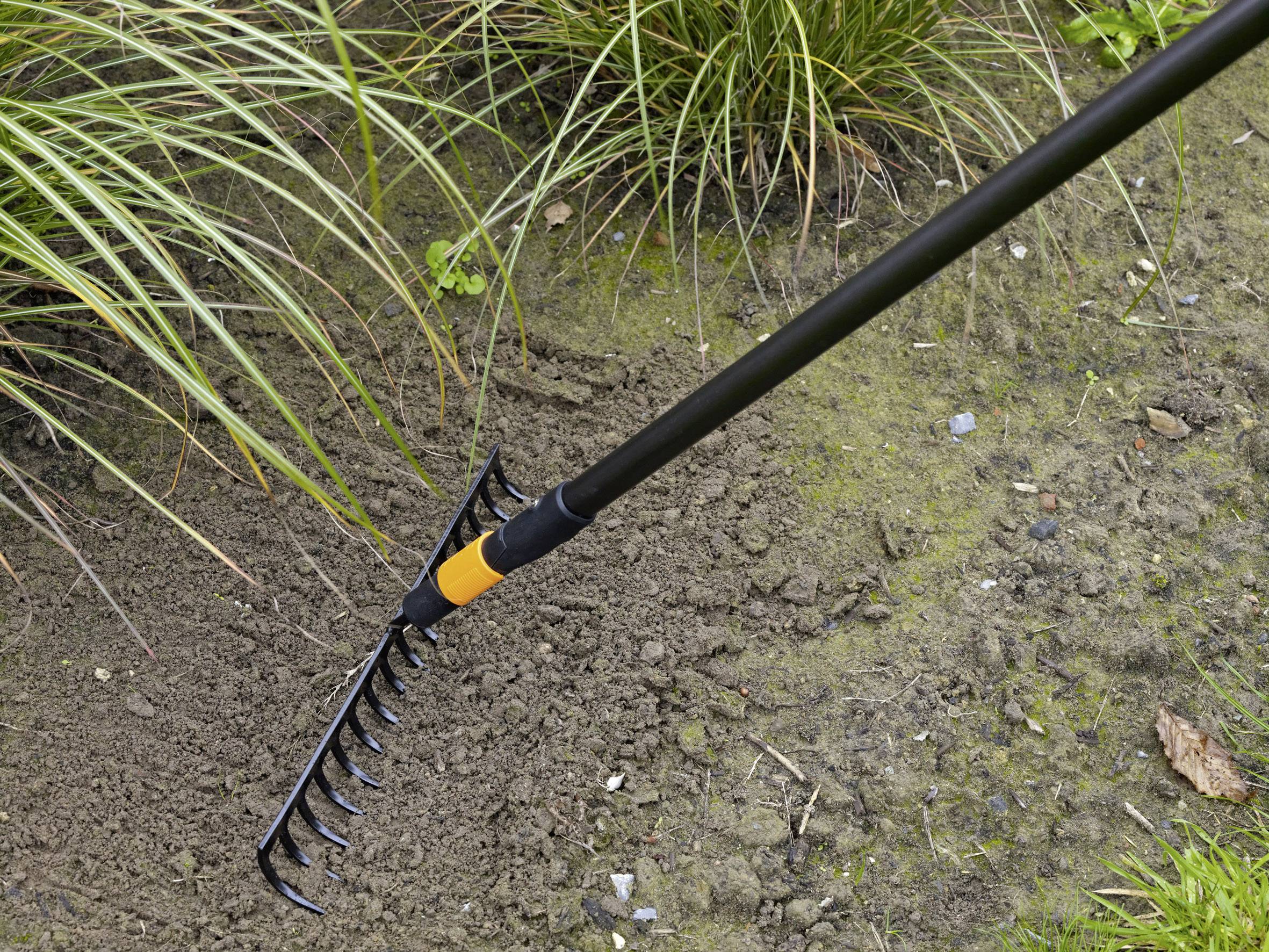 Hrábě upravují půdu v zahradě, obklopené trávou a rostlinami, což ukazuje zahradnickou činnost.