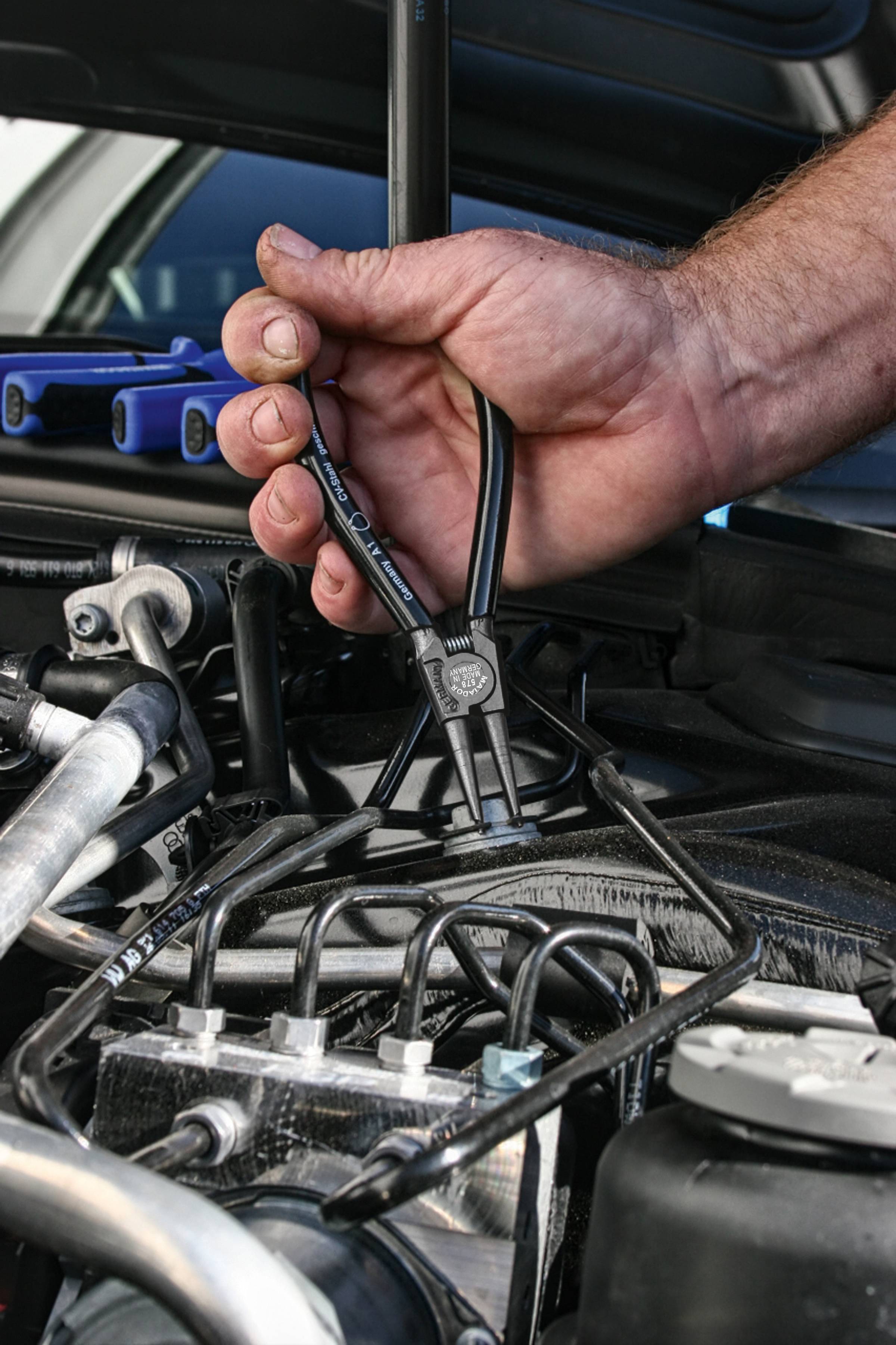 Mechanik používá kleště, aby pracoval na motoru vozidla, přičemž se soustřeďuje na vedení a technické detaily v motorovém prostoru.