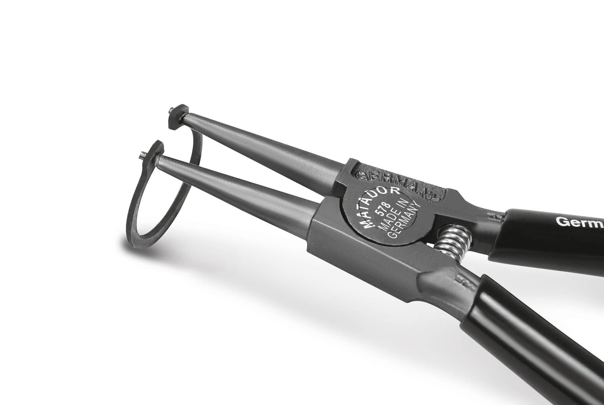 Kleště na pojistné kroužky drží pojistný kroužek. Nástroj má černé rukojeti a šedý hrot.