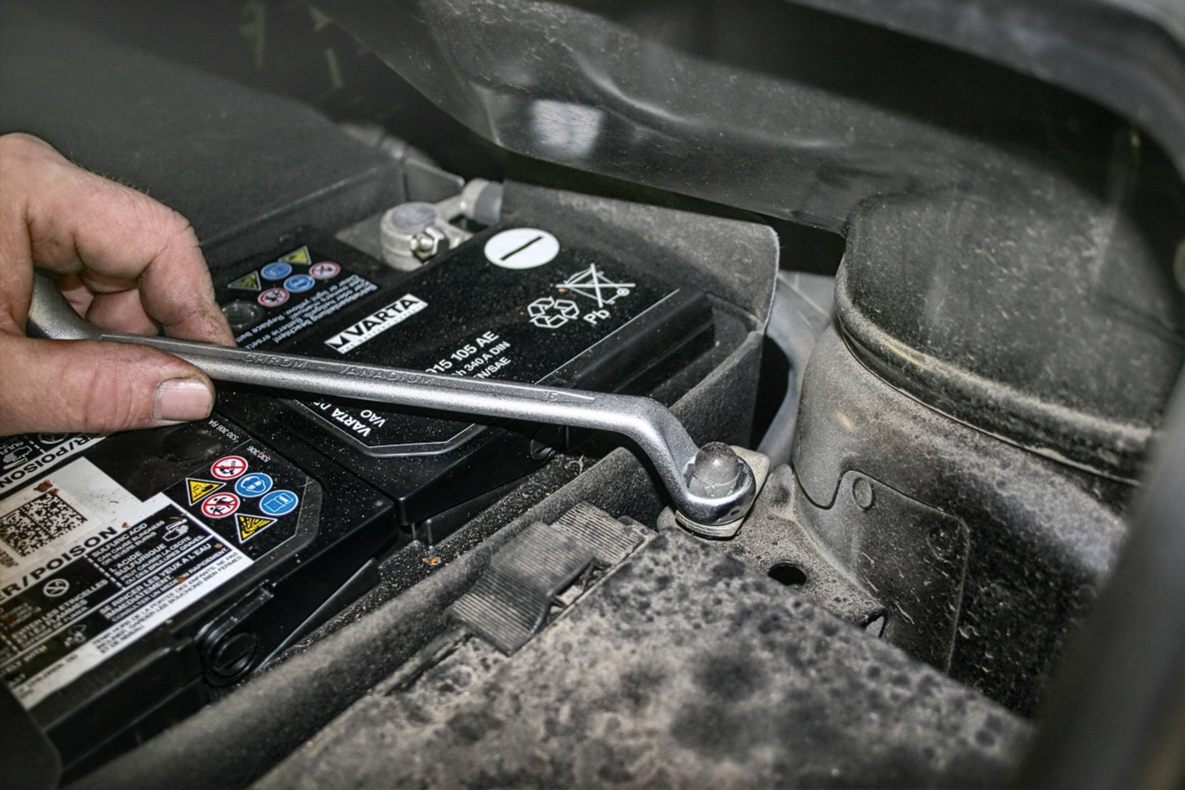 Mechanik utahuje šroub svorky autobaterie pomocí klíče, aby baterii bezpečně upevnil ve vozidle.
