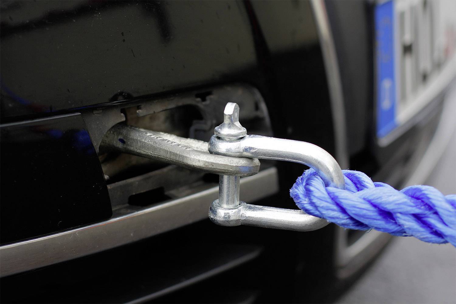 Tažné lano z modrého materiálu je připevněno k přední nárazníku automobilu, připraveno k odtažení vozidla.