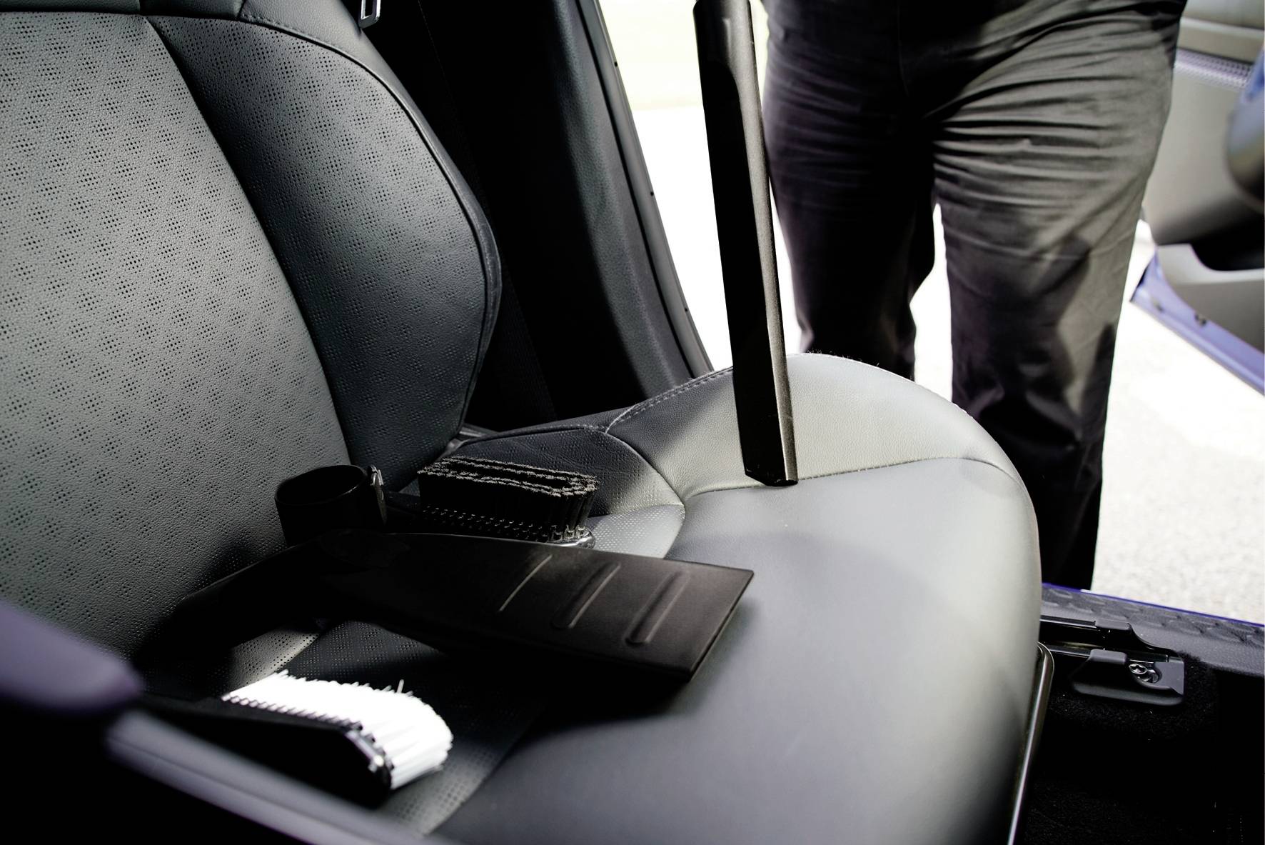 Osoba stojí vedle otevřených dveří automobilu, bezpečnostní pás je na předním sedadle.