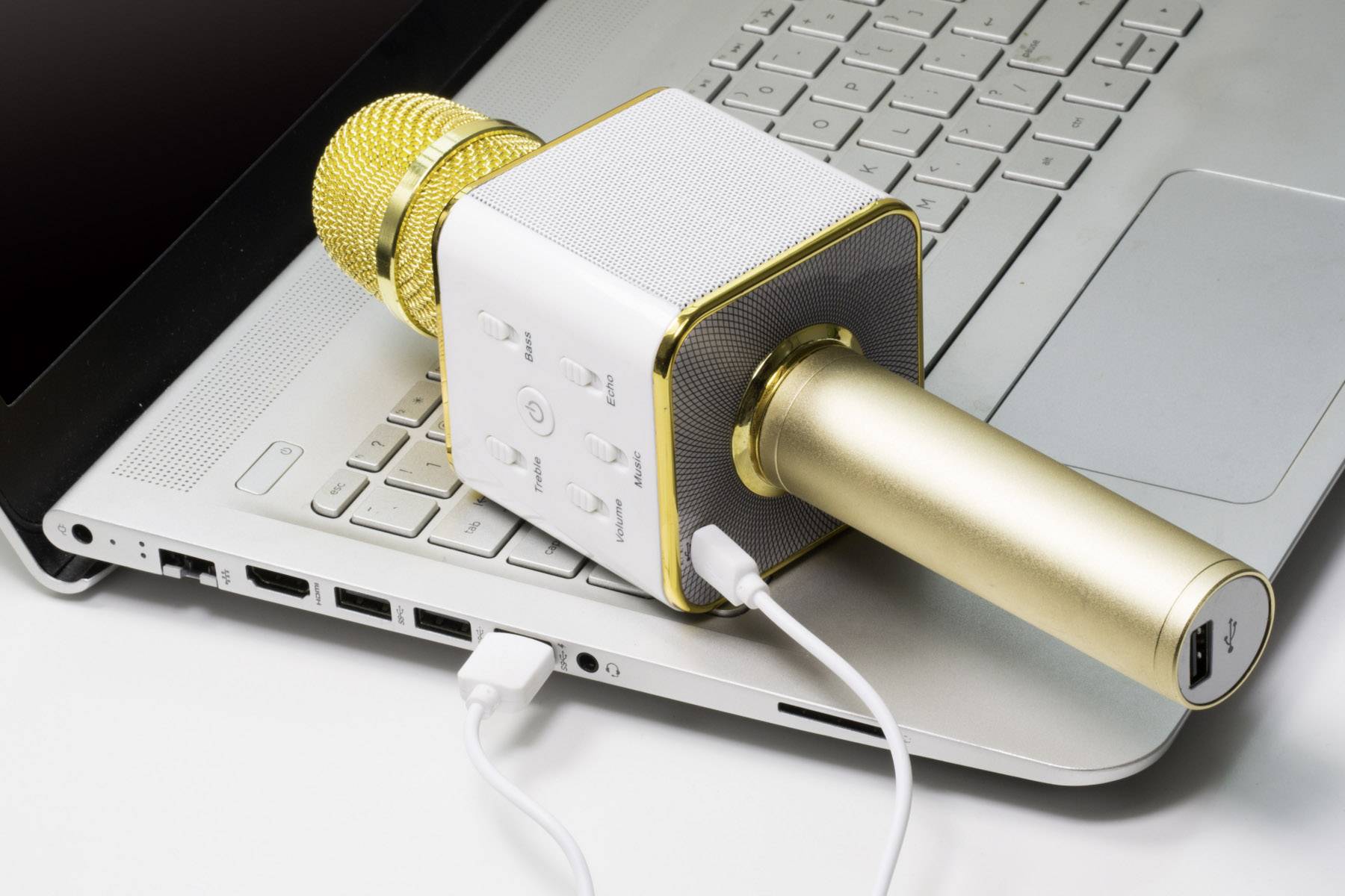 Zlaté mikrofon s připojeným kabelem leží na otevřené klávesnici notebooku, připravené k nahrávání.