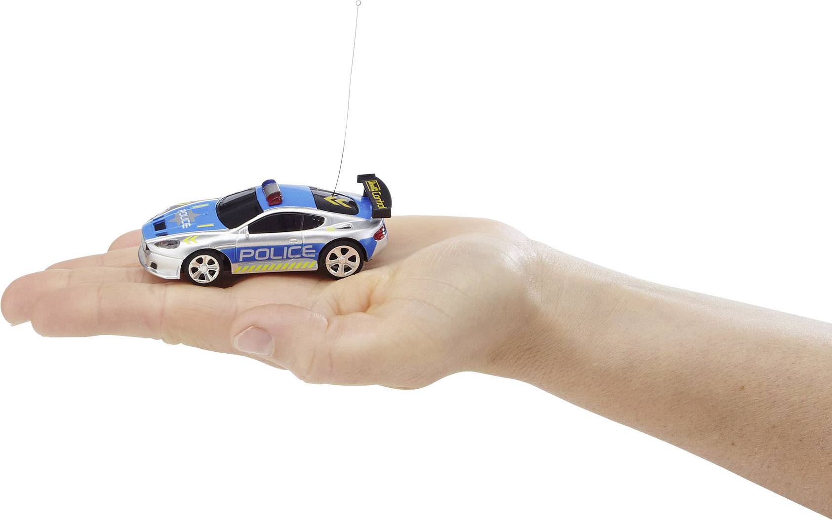 Jedna ruka drží malé, dálkově ovládané hračkářské auto ve stylu policejního vozu s modro-bílým lakováním.