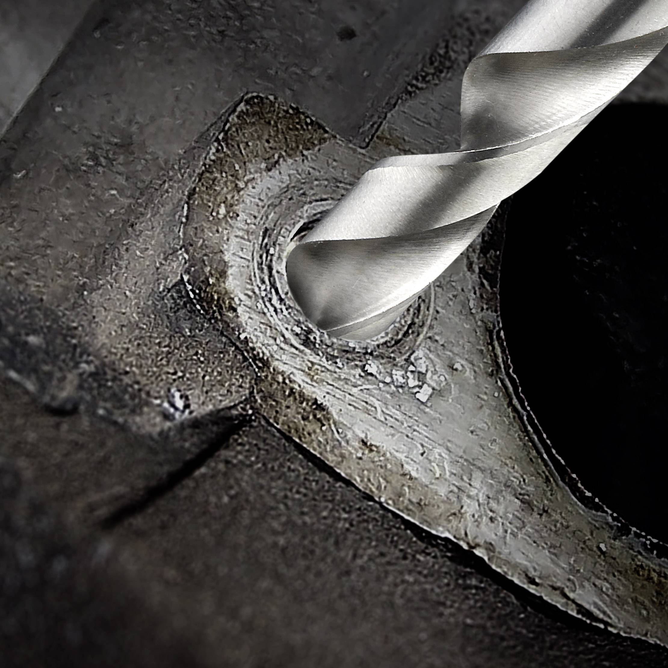 Kovový šroub je vrtán vrtákem do šedého strukturovaného materiálu, detail špičky vrtáku z blízka.