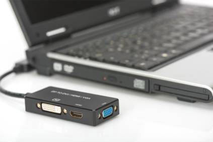 Laptop s připojeným adaptérem s HDMI, DVI a VGA porty leží na stole.