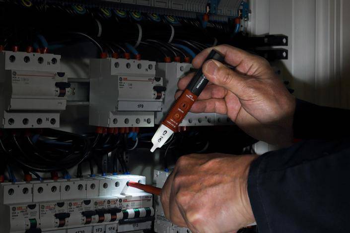 Osoba kontroluje kabely v elektrické rozvodné skříni pomocí bezkontaktního zkoušeče napětí.