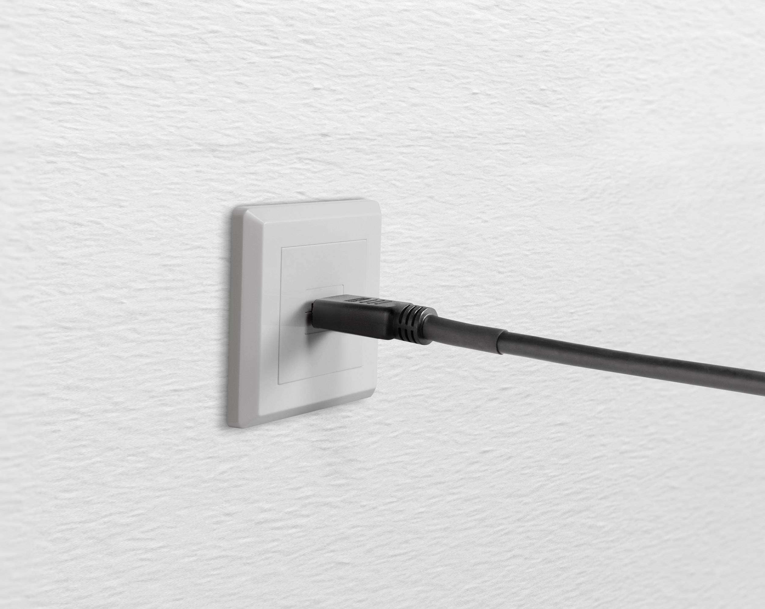 Černý nabíjecí kabel je zapojen do bílé nástěnné zásuvky.