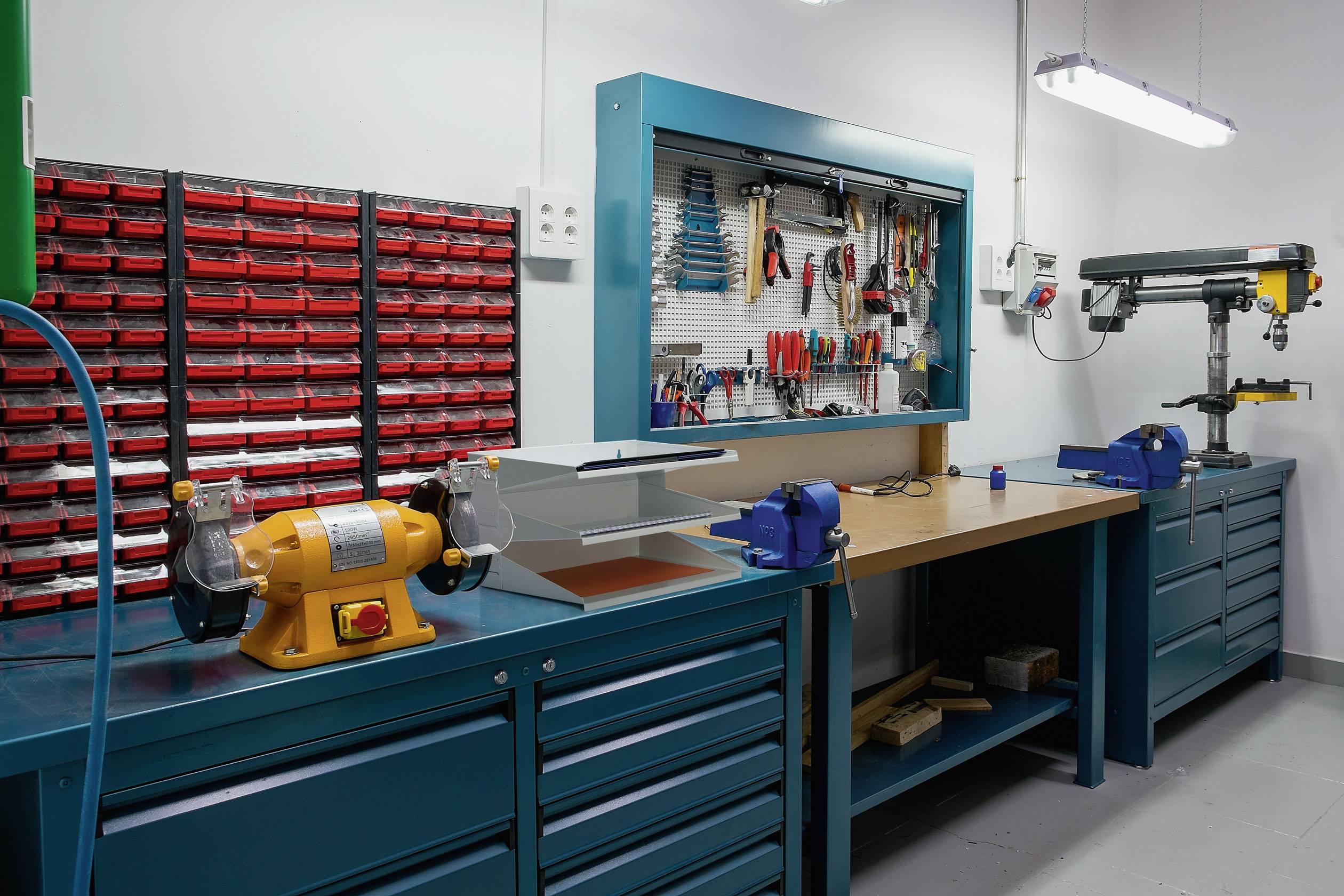 Dílna s pracovním stolem, svěráky, stěnou s nářadím různých druhů ručního náčiní, zásuvkovými skříněmi a stroji.