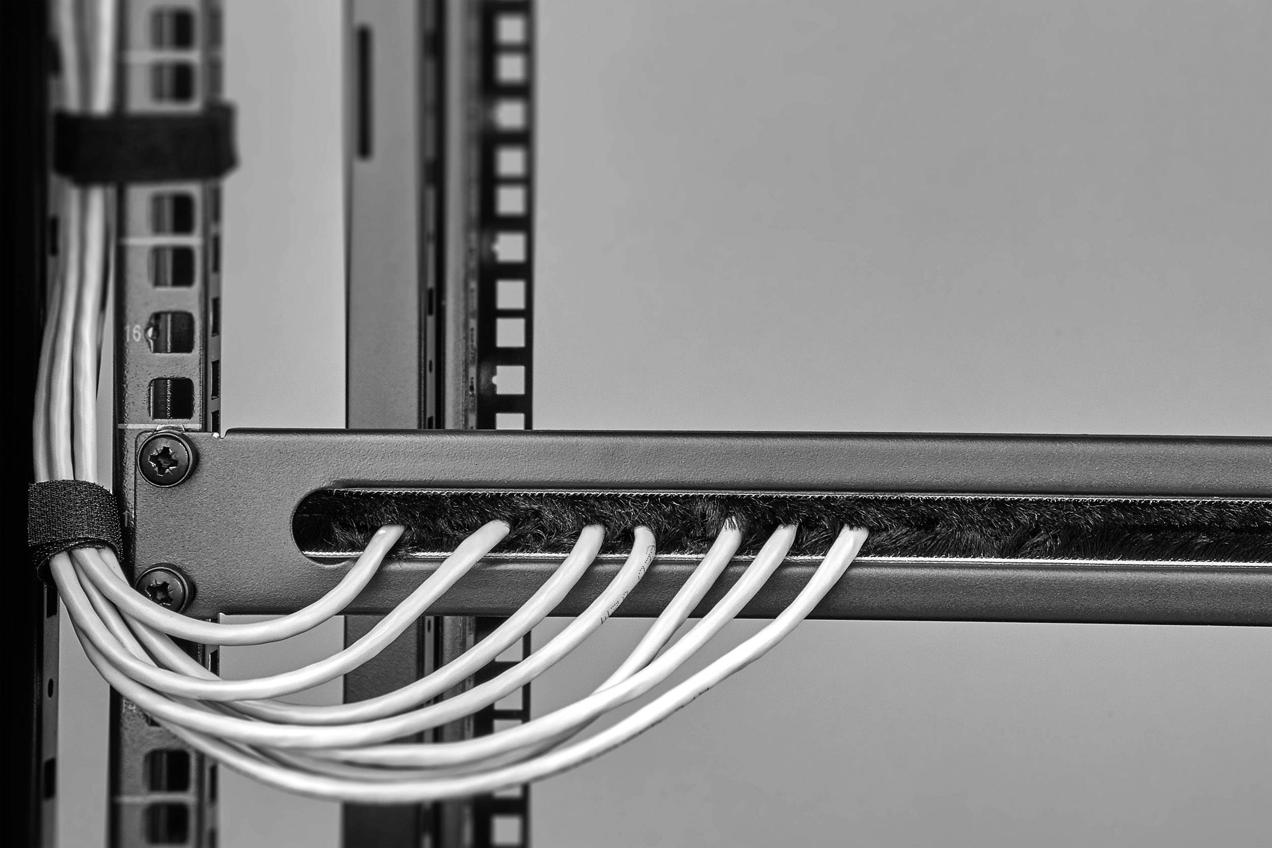 Černobílá fotografie serverové skříně s několika kabely, které jsou uspořádaně vedeny kabelovými průchodkami, ukazuje technickou strukturu a pořádek.