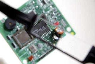 Detailní záběr tištěného spoje s elektronickými komponenty. Lupa zvětšuje část obvodu pro podrobnější prohlédnutí.