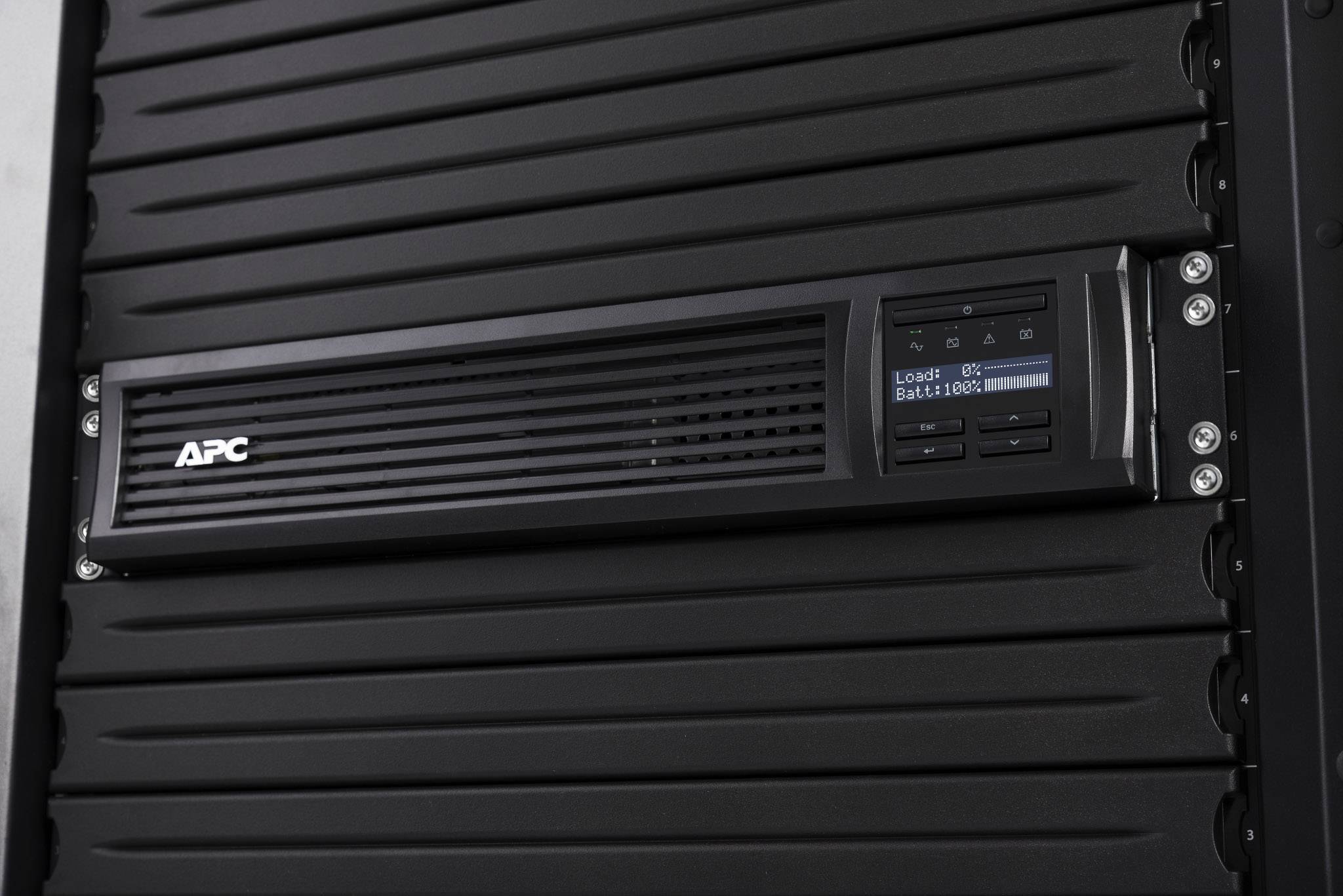Černé zařízení UPS napájecího systému APC v racku serveru. Display zobrazuje stav baterie a zátěže.
