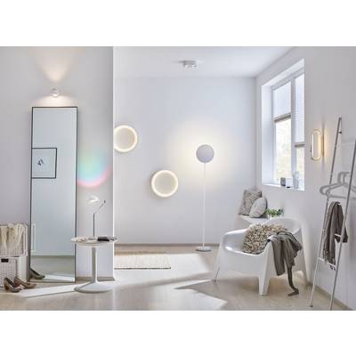 Světlý, moderní obývací pokoj s minimalistickou dekorací. Bílé stěny, stojací a nástěnné lampy, křeslo s polštářem a okno propouštějící denní světlo.
