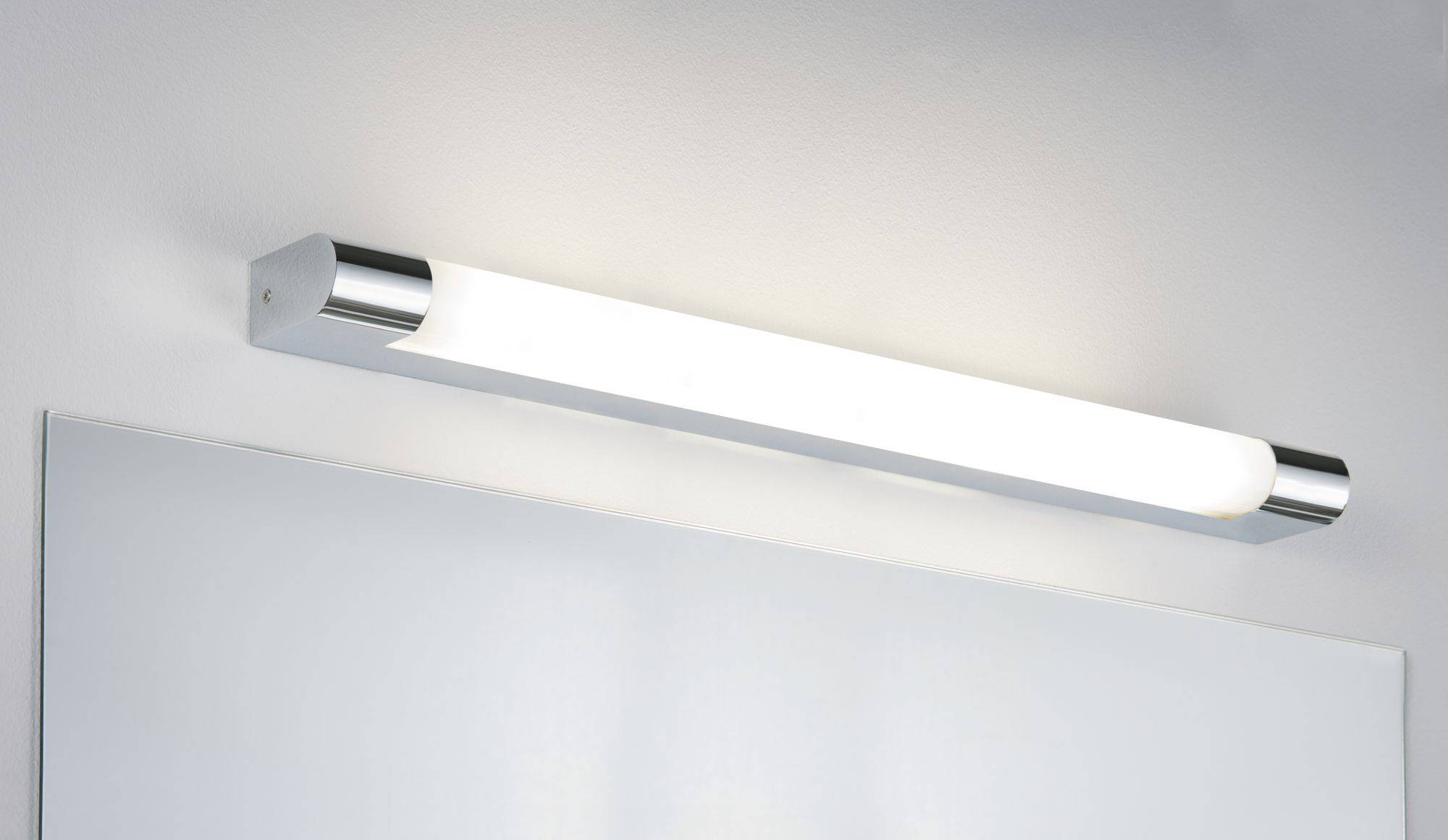 Moderní obdélníková nástěnná lampa s kovovými konci jasně osvětluje zrcadlo na bílé stěně.