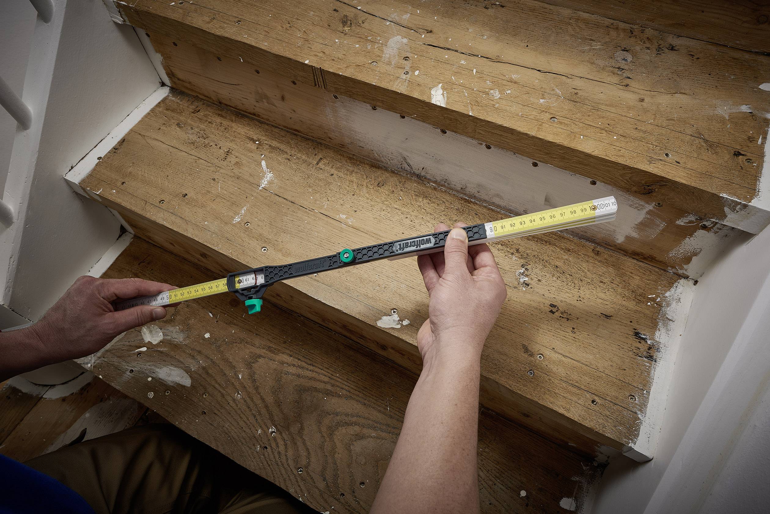 Osoba měří šířku dřevěného stupně měřicím přístrojem, aby provedla renovační práce.