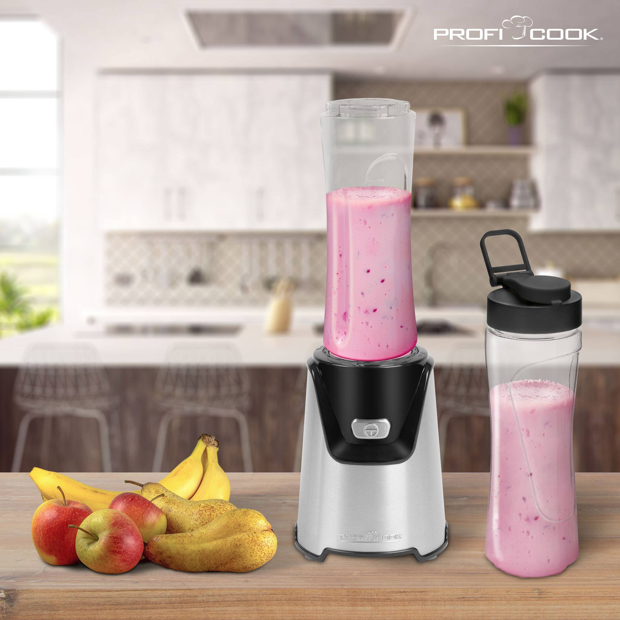 Mixér s růžovým smoothie stojí na kuchyňské pracovní desce. Vedle něj leží čerstvá jablka a banány. V pozadí je moderní kuchyně.