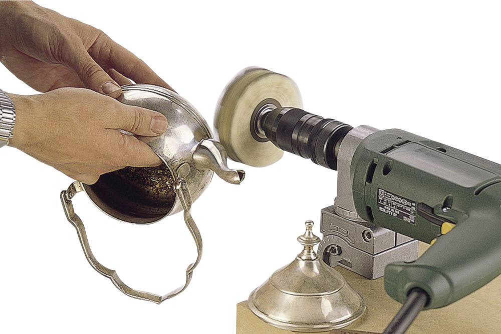 Člověk leští stříbrnou konvici pomocí elektrické leštičky. Víko konvice leží vedle.