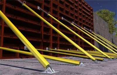 Žluté vzpěry zajišťují červenou stavební stěnu, která se táhne podél betonové plochy.