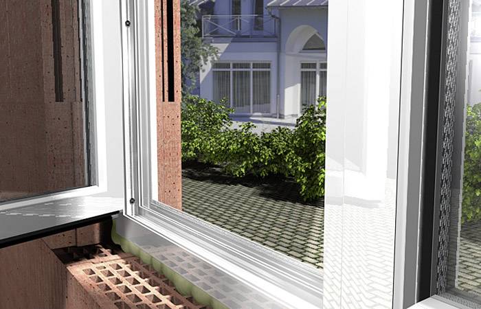 Otevřené okno v budově, skrz které je vidět dvůr s zelenými keři a protější dům.