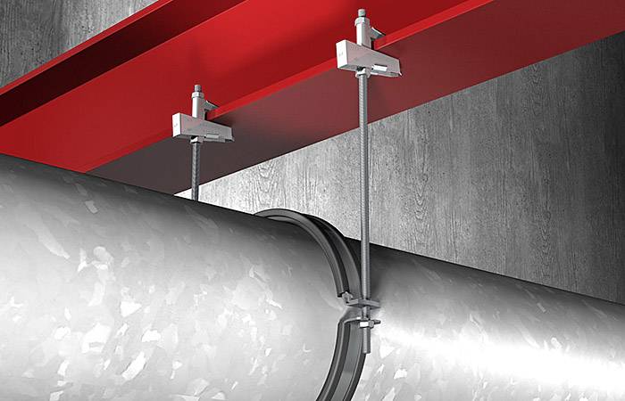 Velký kovový potrubní rozvod upevněný pomocí svorek ke konstrukční ocelové konstrukci červené barvy.