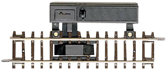 Výhybka na kolejích modelové železnice, zobrazená v detailním záběru, s mechanickým ovládacím zařízením nad kolejnicemi.