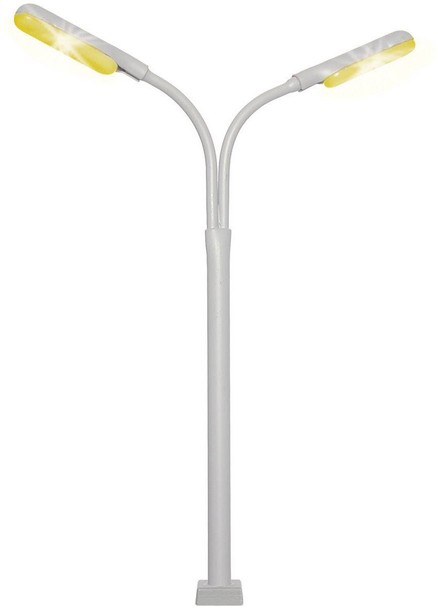 Moderní pouliční lampa se dvěma vnějšně nakloněnými svítidly, která vyzařují žluté světlo, stojí před bílým pozadím.