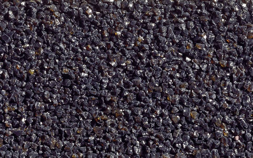 Detailní záběr textury složené z mnoha malých, tmavých kamenů nebo zrn, které jsou těsně vedle sebe a vytvářejí nepravidelný povrch.