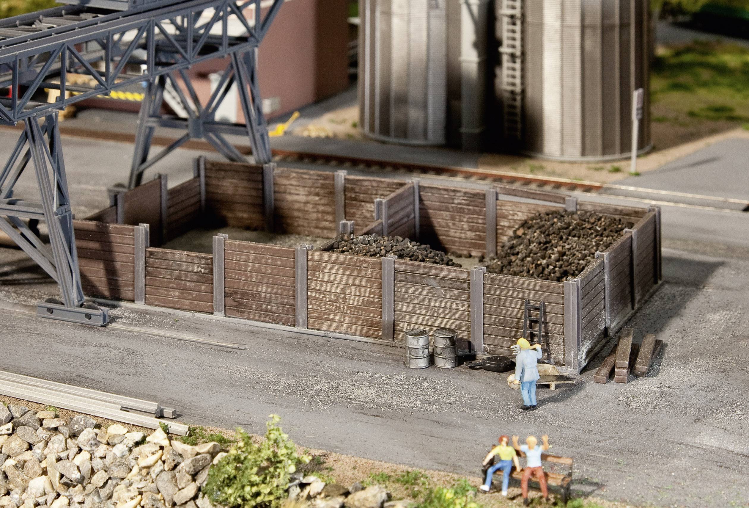 Miniatura zobrazuje uhelný sklad s dřevěnými zátarasy. Dvě figurky sedí na lavičce v popředí, zatímco další stojí u skladu.