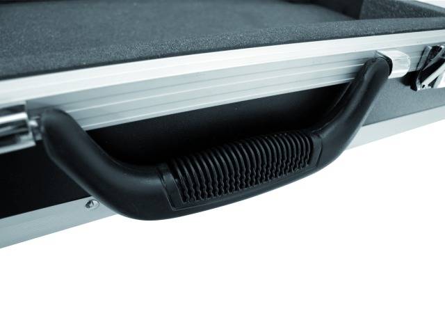 Detailní záběr černé plastové rukojeti na hliníkovém kufříku, který leží na ploché ploše.