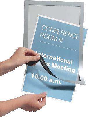 Ruka mění štítek v stříbrném rámu. Na štítku stojí 'Konferenční místnost III, Mezinárodní obchodní schůzka, 10:00 hod.'.