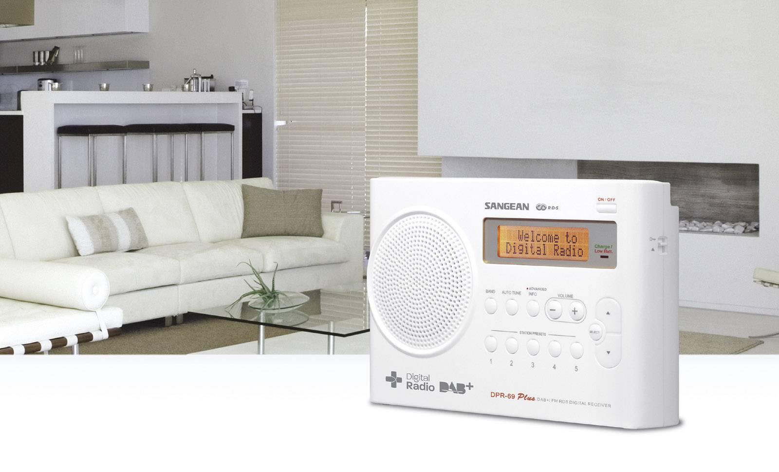 Digitální rádio stojí na stole v moderně zařízeném obývacím pokoji. Na displeji je napsáno 'Vítejte v digitálním rádiu'.