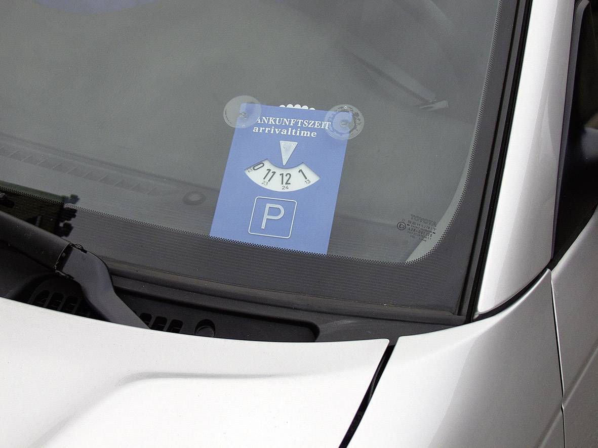 Modrý parkovací kotouč umístěný za čelním sklem automobilu ukazuje čas příjezdu 11:30.