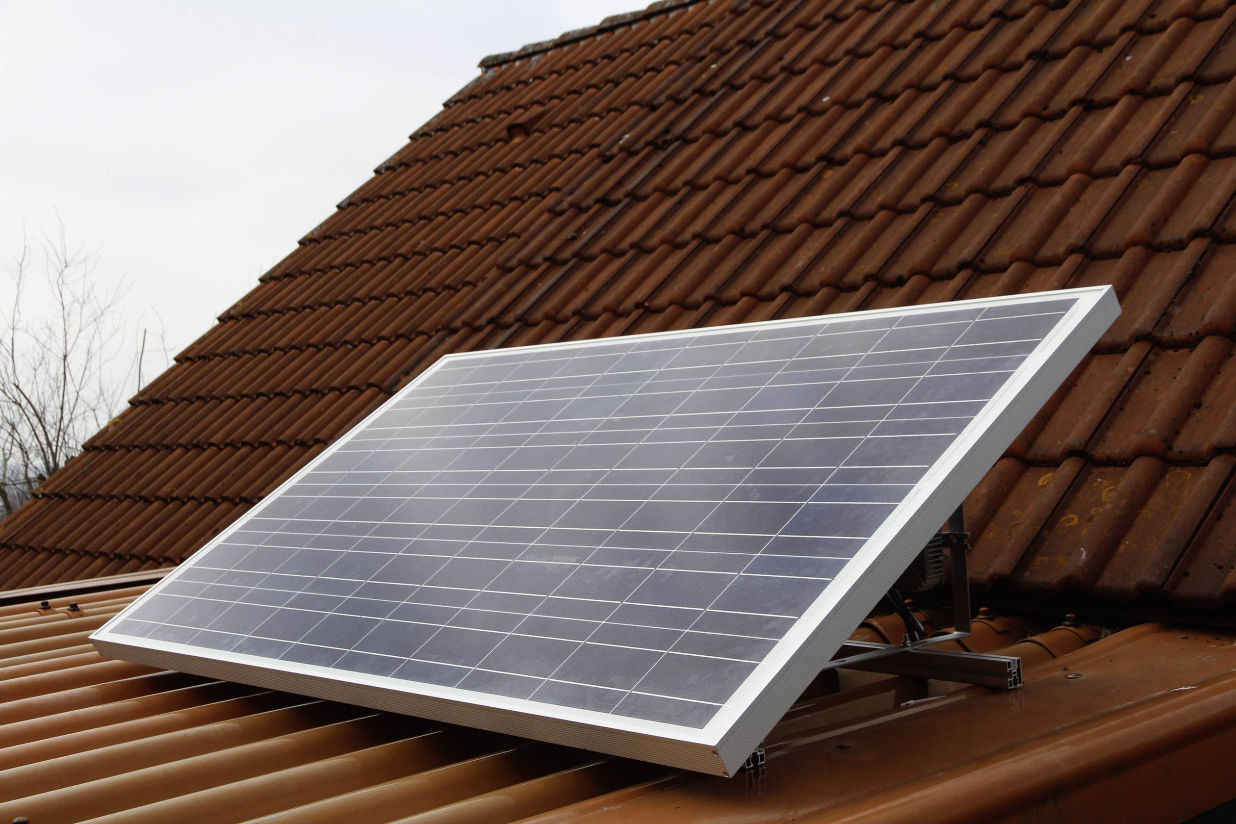 Solární panel na střešní tašce, který se používá k výrobě elektřiny. V pozadí jsou holé stromy.