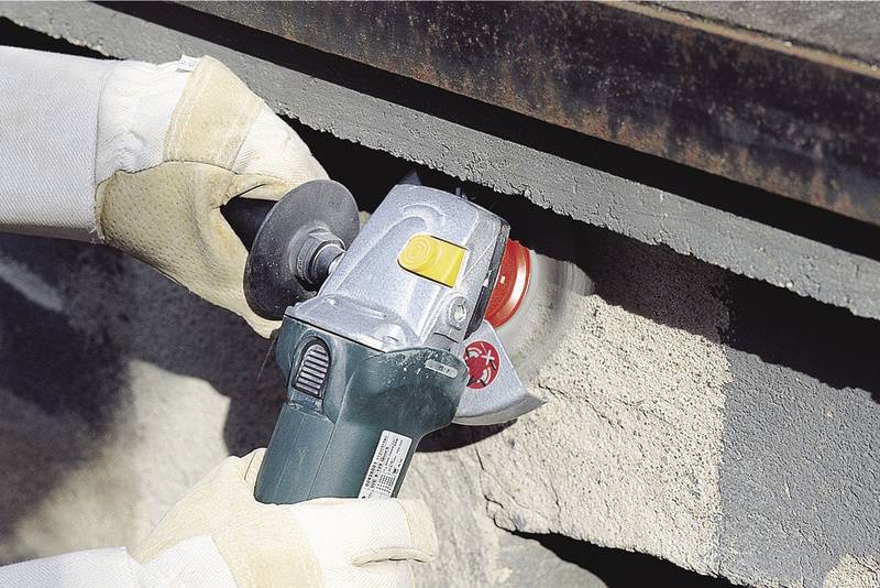 Řemeslník brousí beton úhlovou bruskou, je oblečen v ochranných rukavicích.