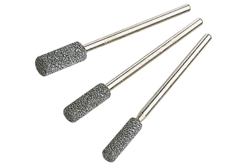 Tři válcové brusné hroty z šedého materiálu s kovovými rukojeti, uspořádané podle velikosti, na bílém pozadí.