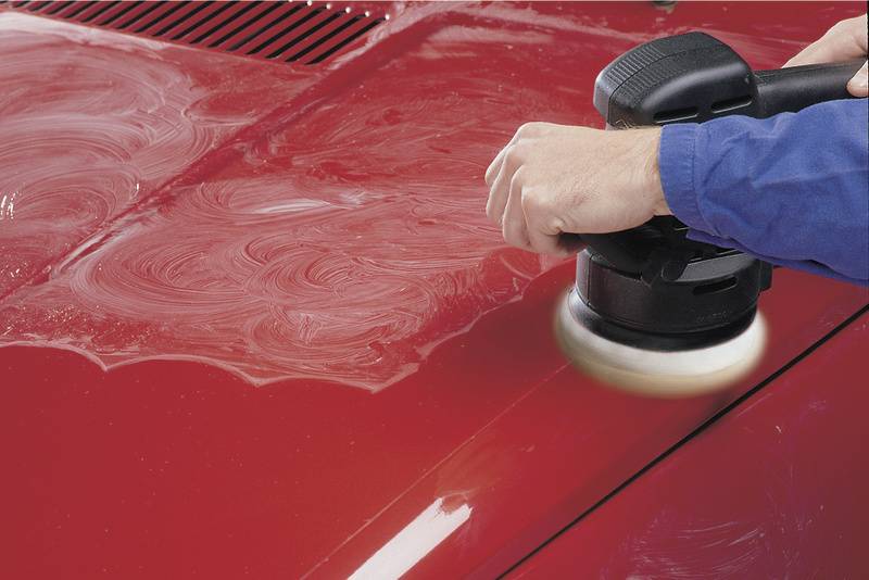 Jedna osoba leští červenou karoserii automobilu pomocí elektrické leštičky.