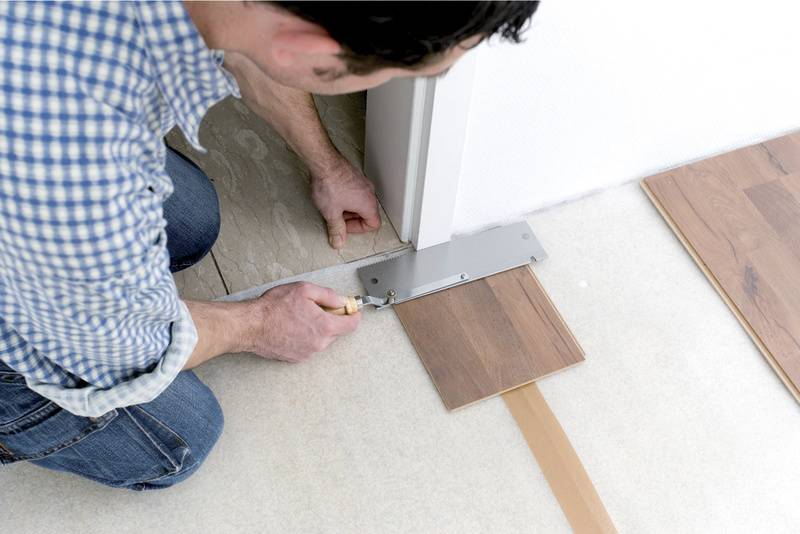 Muž řeže kus laminátu nástrojem v blízkosti dveří, aby jej přesně zakomponoval.