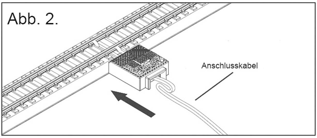 Obrázek modelářské železniční koleje s připojovacím kabelem ústícím do obdélníkového adaptéru. Šipka ukazuje na adaptér.