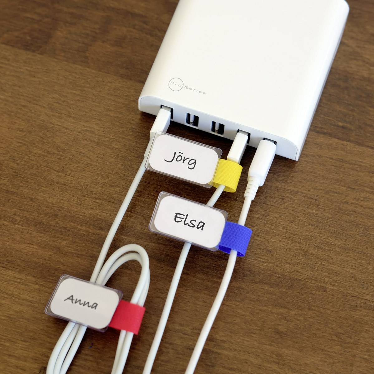 Tři kabely jsou připojeny k nabíječce. Každý kabel je označen barevnou nálepkou: 'Jörg', 'Elsa', 'Anna'.