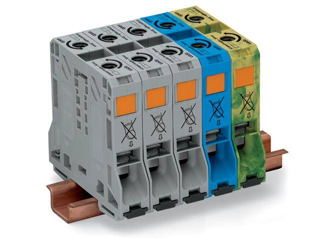 Čtyři elektrické jističe namontované na kolejnici v šedé, modré a zelené barvě. Zařízení jsou určena pro jištění elektrických obvodů.