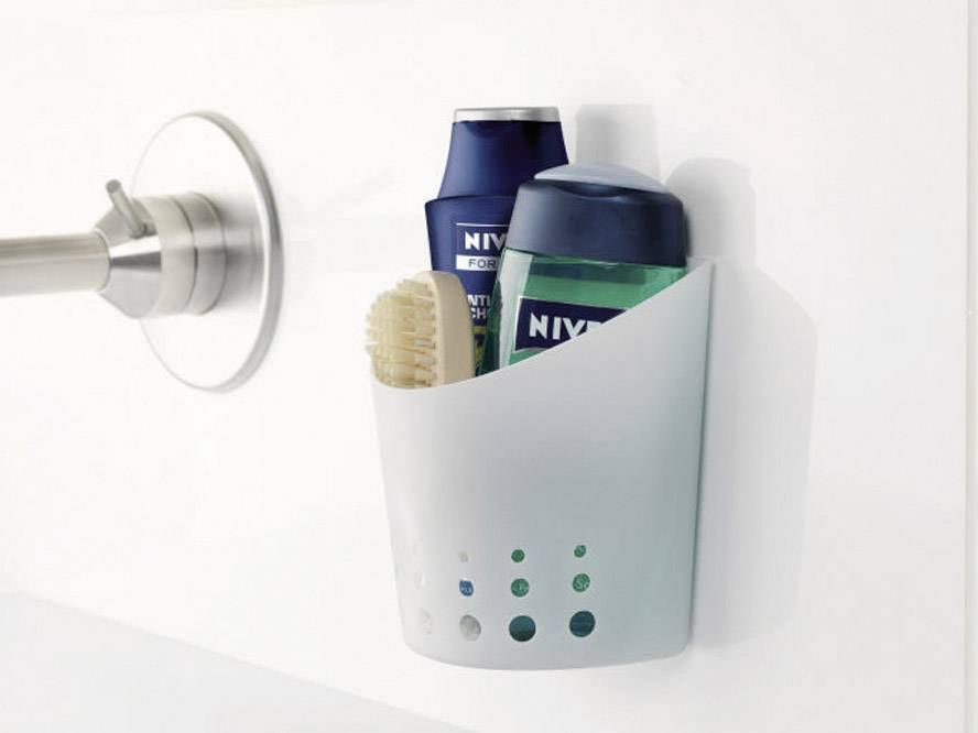 Dva výrobky Nivea a kartáč v bílém sprchovém košíku zavěšené na stěně koupelny.