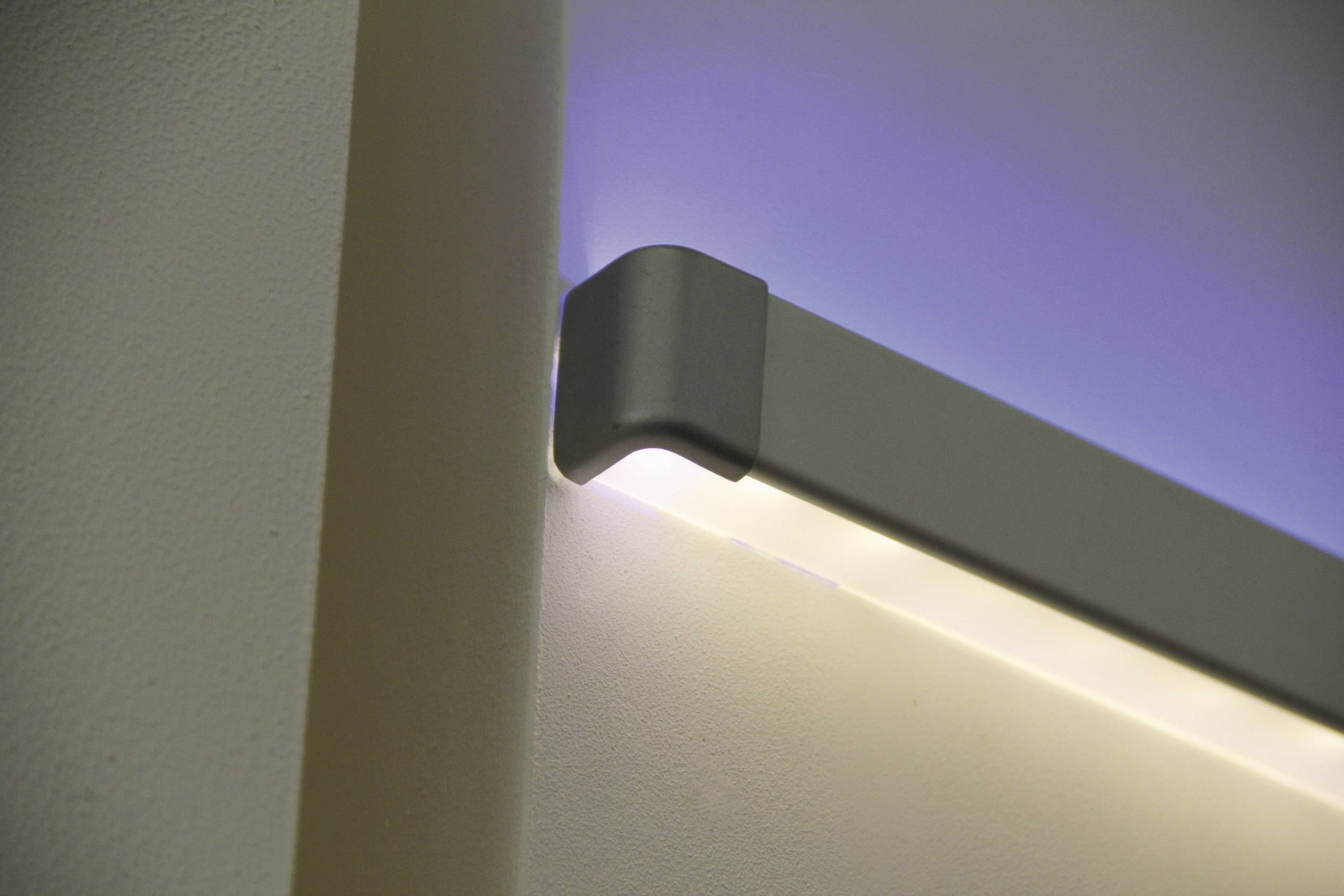 Moderní, minimalistické nástěnné světlo s nepřímým osvětlením, namontované na béžové stěně. Vyzařuje modrobílé světlo.